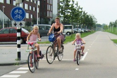 A mother and her two young daughters ride their bikes on a wide cycle path