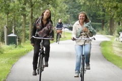 Two women ride bikes side-by-side, laughing as they go