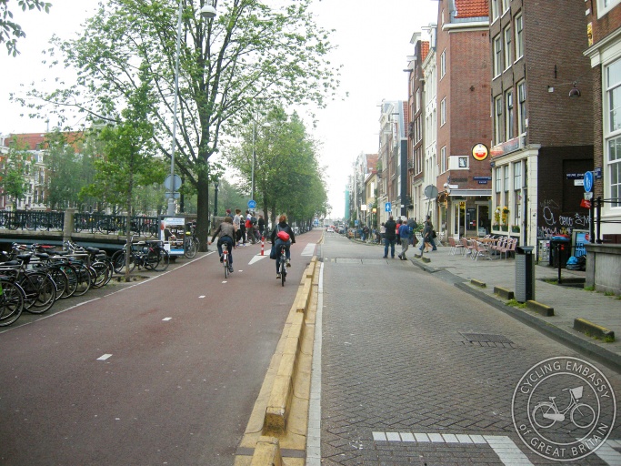 A photo of Geldersekade in Amsterdam. On the left is a wide two-way cycle path. On the right is a one-way road for cars.