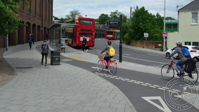 Cyclists riding behind a bus stop shelter on a bus stop bypass cycle track, Vogue gyratory, Brighton